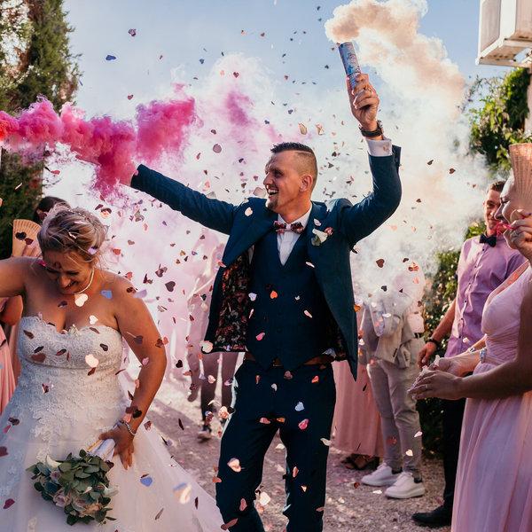 Groupe de témoins et fumigènes roses à la sortie du mariage